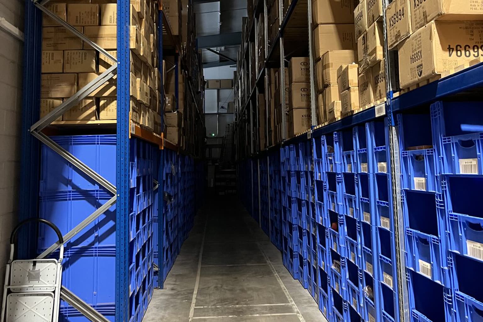 Warehouse aisle with racking, boxed stock and blue storage bins for e-commerce fulfilment